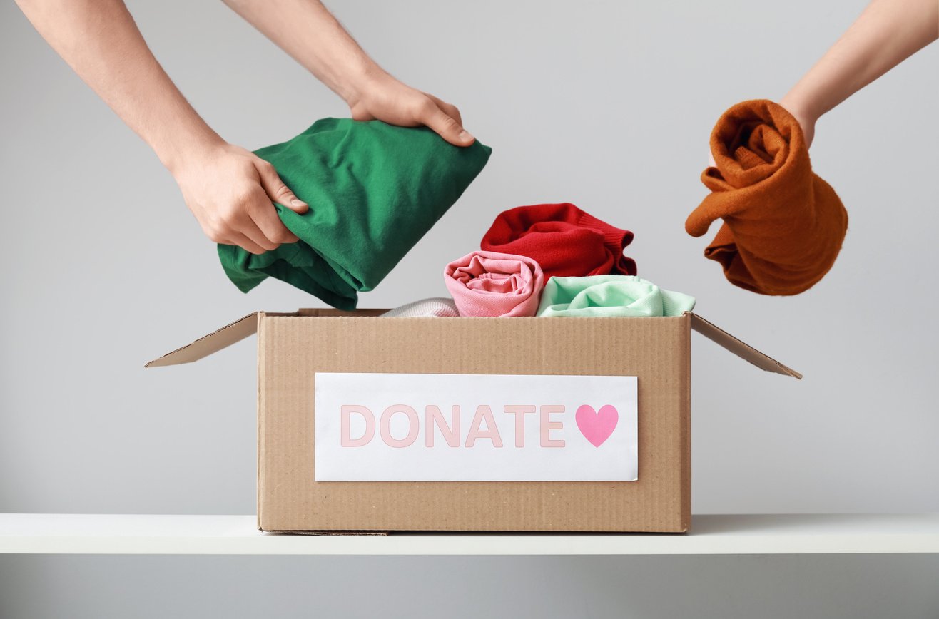 Women Putting Donation Clothes in Box on Shelf against Light Background