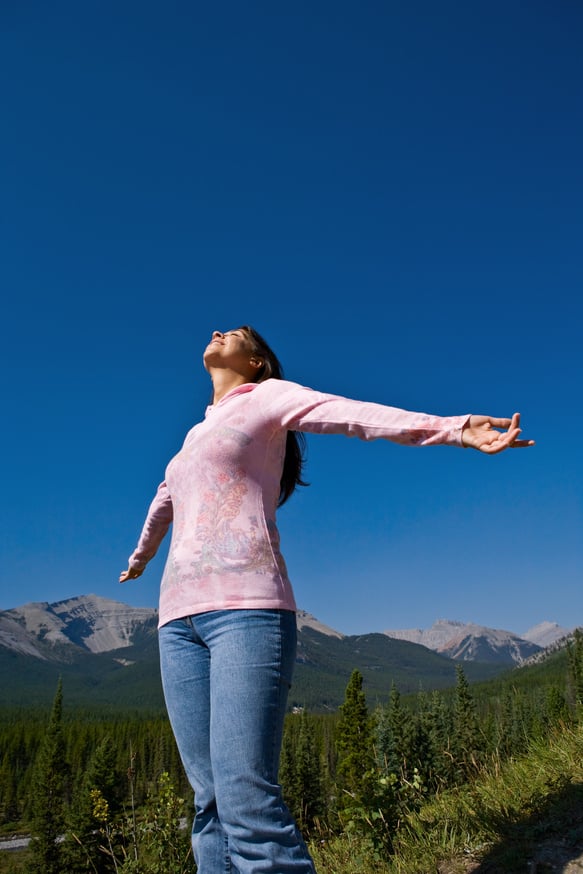 Female in mountain area gesturing with arms outreached looking up